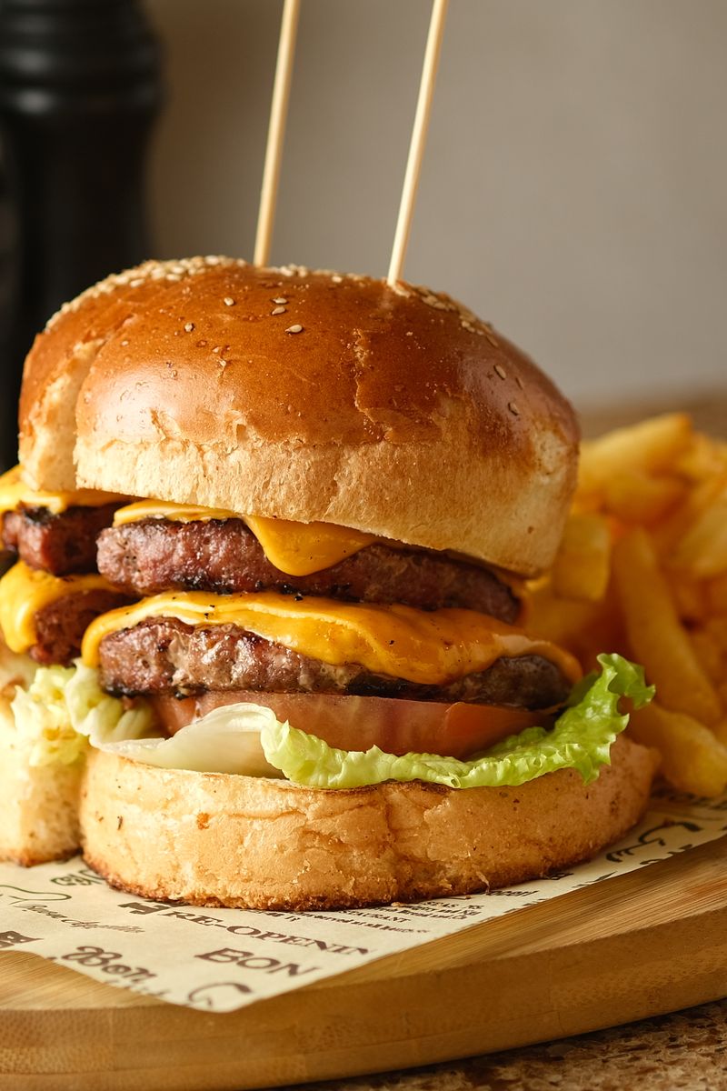Juicy cheeseburger with double patties and fries served on a wooden board.